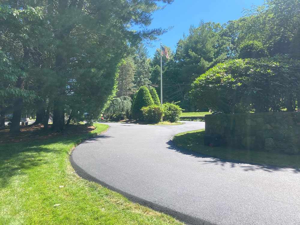 Freshly paved asphalt driveway through landscaped yard showing driveway paving services in Cranston