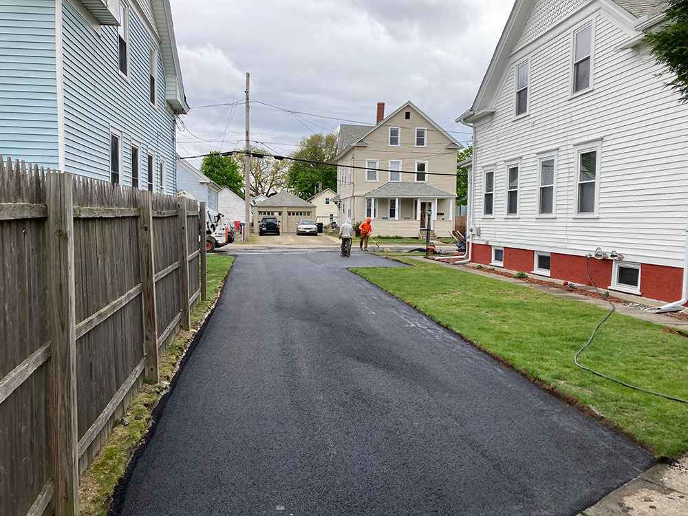 Fresh asphalt driveway between homes showing professional residential paving services in Cranston